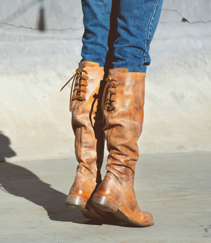 A person donning a pair of Bed Stu Manchester boots, exhibiting transitional style in their tall brown footwear.