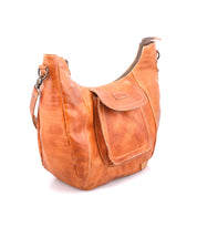 The Bed Stu Manitoba is a brown handcrafted bag featuring an external front pocket, zipper closure, and adjustable strap, shown against a white background.