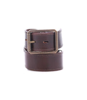 The Bed Stu Meander is a rugged belt made from brown distressed leather featuring visible stitching and a rectangular antique metal buckle. The brand name "Bed Stu" is engraved near the coiled buckle.