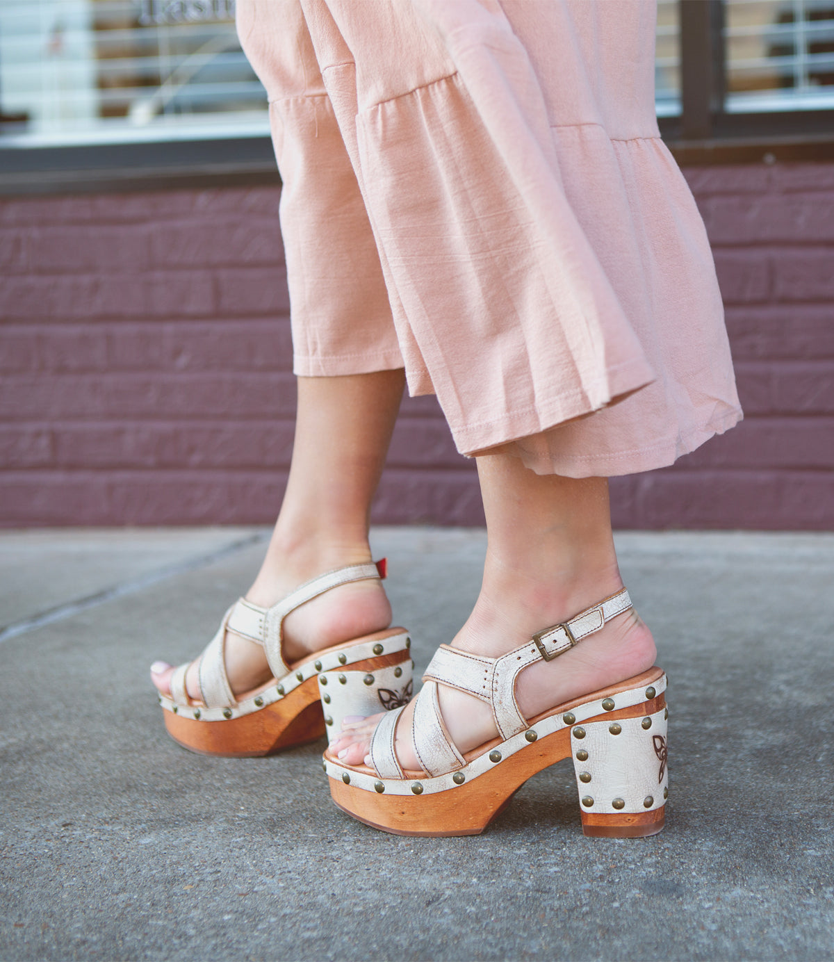 Woman standing on a sidewalk wearing pink pants and comfortable, Bed Stu stud-detailed sandals.