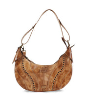 The Megara by Bed Stu is a brown leather saddle bag featuring decorative stitching and metal studs. It comes with an adjustable strap, leather details, and proudly displays the brand logo on the front.
