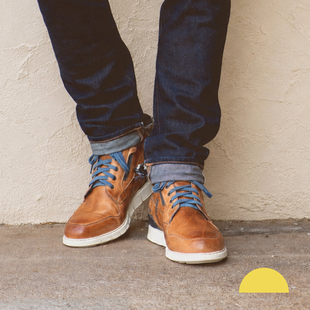 Person wearing brown leather lace-up ankle boots with blue laces, white soles, and dark cuffed jeans.