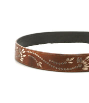 The Bed Stu Mohawk is a women’s belt made from brown distressed leather, featuring silver floral and leaf embossing, shown in a circular layout on a white background.