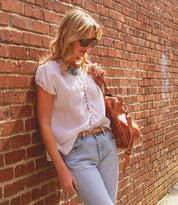 Woman in casual attire leaning against a brick wall, accented by her Bed Stu Monae II premium leather belt with customizable buckle.