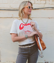 Woman in a casual outfit with a graphic t-shirt and striped trousers, accessorized with sunglasses, a watch, a Bed Stu Monae II premium leather belt with hand-stamped details, and a shoulder bag, standing against a