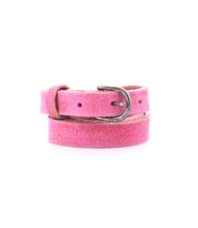 The Bed Stu Monae is a pink skinny leather belt with a distressed texture and silver buckle, coiled on a white background—ideal for adding a boho touch to your outfit.