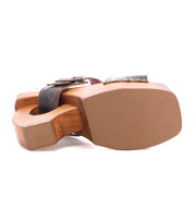 The Bed Stu Mutable is a wooden sandal lying on its side, featuring a decorative buckle and cutout heel design that showcases its vintage influence and wooden platform heel.