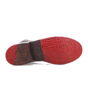 The underside of a brown leather Bed|Stü Nandi Chelsea boot with a prominent red rubber sole featuring embossed text and a textured heel.