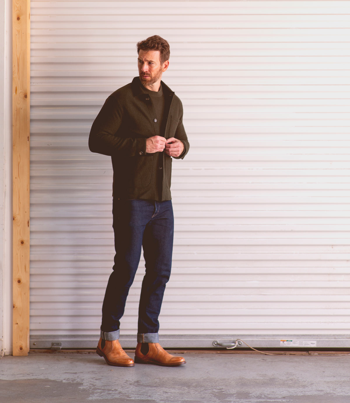 A man wearing timeless Bed Stu Nando leather ankle boots stands in front of a garage door.