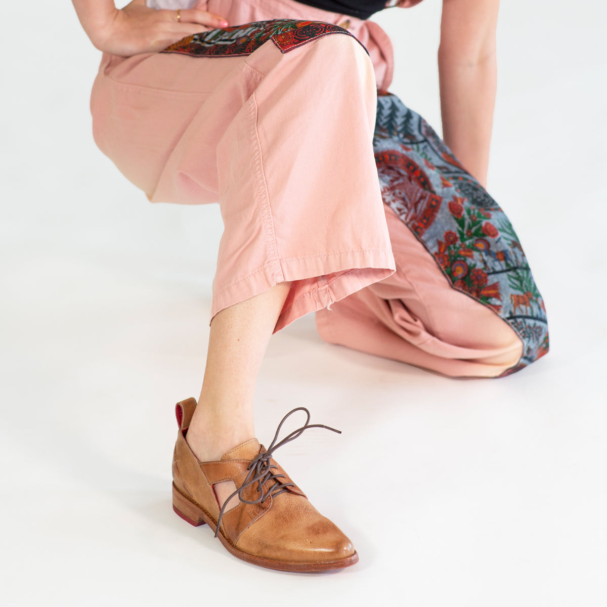 Woman in Neftis cropped pink trousers and a Bed Stu brown lace-up shoe with a pointed toe posing against a white background.