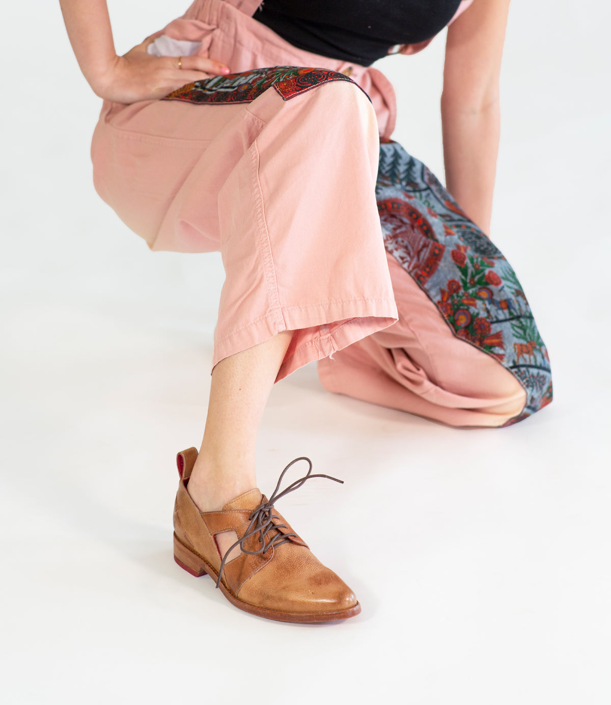 Woman in Neftis cropped pink trousers and a Bed Stu brown lace-up shoe with a pointed toe posing against a white background.