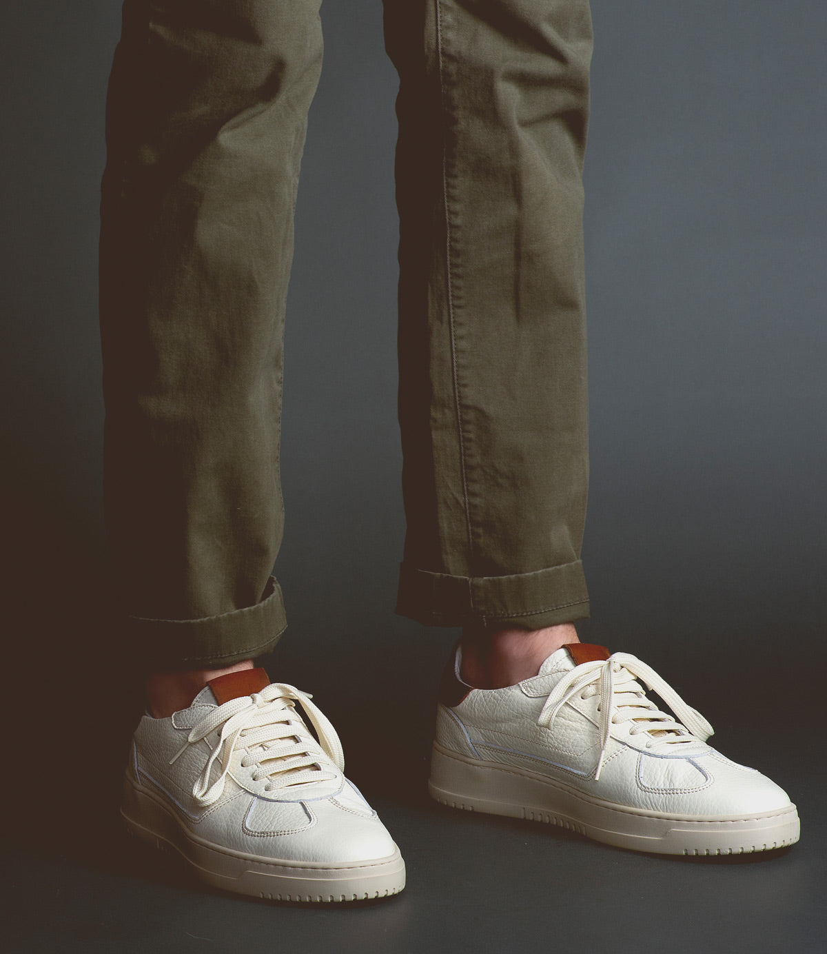A person wearing olive green pants and North sneakers by Bed Stu, known for their high-quality leather, stands against a dark background.