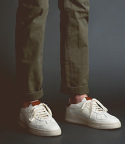 A person wearing olive green pants and North sneakers by Bed Stu, known for their high-quality leather, stands against a dark background.