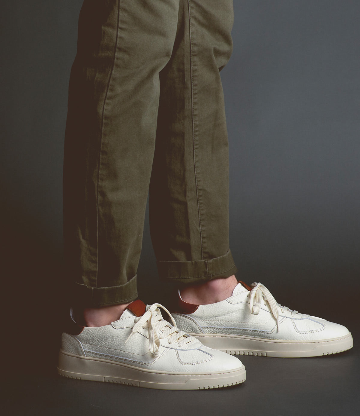 Person wearing green pants and Bed Stu North sneakers standing against a dark background.