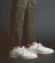 Person wearing green pants and Bed Stu North sneakers standing against a dark background.