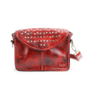 The Bed Stu Occurrence is a red leather crossbody bag with a studded flap, an adjustable strap, and a small rectangular logo in the lower right corner.