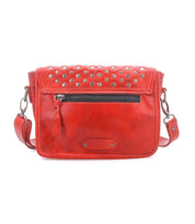 The Bed Stu Occurrence is a red leather compact crossbody with a front zip pocket, metal studs on the flap, and an adjustable strap—ideal when you want clutch style plus crossbody versatility.