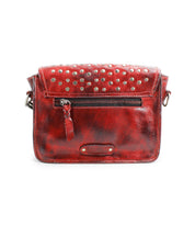 The Occurrence by Bed Stu is a red leather crossbody bag featuring metal studs, a front zipper pocket, and an adjustable strap.