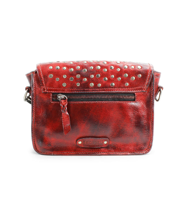 The Occurrence by Bed Stu is a red leather crossbody bag featuring metal studs, a front zipper pocket, and an adjustable strap.