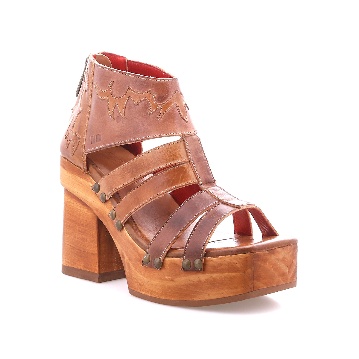 The Bed Stu Orphyx is a brown leather open-toe sandal featuring strappy details, metal studs, a thick wood platform block heel, and a back zipper closure.