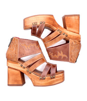 The Bed Stu Orphyx sandals feature chunky brown leather straps, wood platform heels, open-toe design, decorative stitching, and metal studs, shown in side view against a white background.