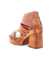 The Orphyx by Bed Stu is a brown leather open-toe sandal featuring decorative stitching, metal rivets, leather straps, a thick wood platform heel, and a back zipper.