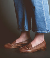 A person wearing blue jeans and classic style brown Bed Stu Paris loafers.