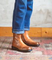 A person wearing jeans and Bed Stu Italian leather boots standing on a rug.