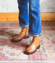 A woman wearing Bed Stu Italian leather boots standing on a rug.