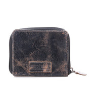 A worn black compact leather wallet by Bed Stu, called Plus, featuring visible creases, a front rectangular embossed patch, and a zippered coin pocket.