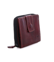 The Bed Stu Plus is a compact brown leather wallet with contrast stitching, snap closure, and edge zippered coin pocket, shown standing upright on a white background.