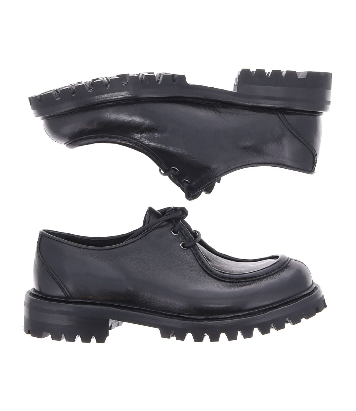 Two Portare shoes by Bed Stu in black leather, featuring thick, rugged soles, are presented vertically with the soles touching against a white background. These vintage-inspired pieces, crafted in an Italian factory, infuse a 90s edge with timeless style and modern durability.