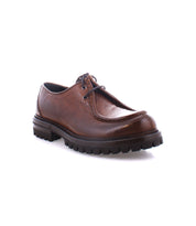 The Portare boot by Bed Stu, a single brown leather moc-toe lace-up design with a rugged sole, displays its vintage-inspired style against a white background.