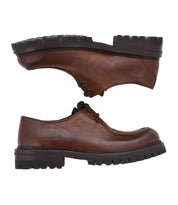 The Portare boots by Bed Stu are crafted in an Italian factory, featuring brown leather with moc-toe stitching, black laces, and chunky black soles that exude a vintage-inspired style.