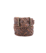 The Bed|Stü Proem belt, handwoven in rich brown leather with a vintage metal buckle, is coiled neatly against a plain white background, highlighting its exquisite artisan craftsmanship.