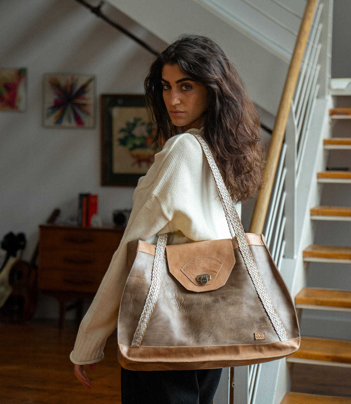 A woman carrying a Bed|Stü Proper, a large two-toned vegetable-tanned leather tote bag with handwoven straps and a metal turn-lock closure.