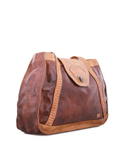 The Proper tote bag by Bed|Stü is crafted from brown vegetable-tanned leather with braided accents and handwoven straps, featuring a tan flap closure, visible stitching, and an interior lined with organic cotton. It is displayed against a white background.