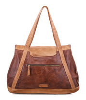 The Bed|Stü Proper is a brown vegetable-tanned leather tote bag with handwoven, braided handles, a front zippered pocket, and tan accents along the top edge and handles. It features an organic cotton-lined interior and is shown against a white background.