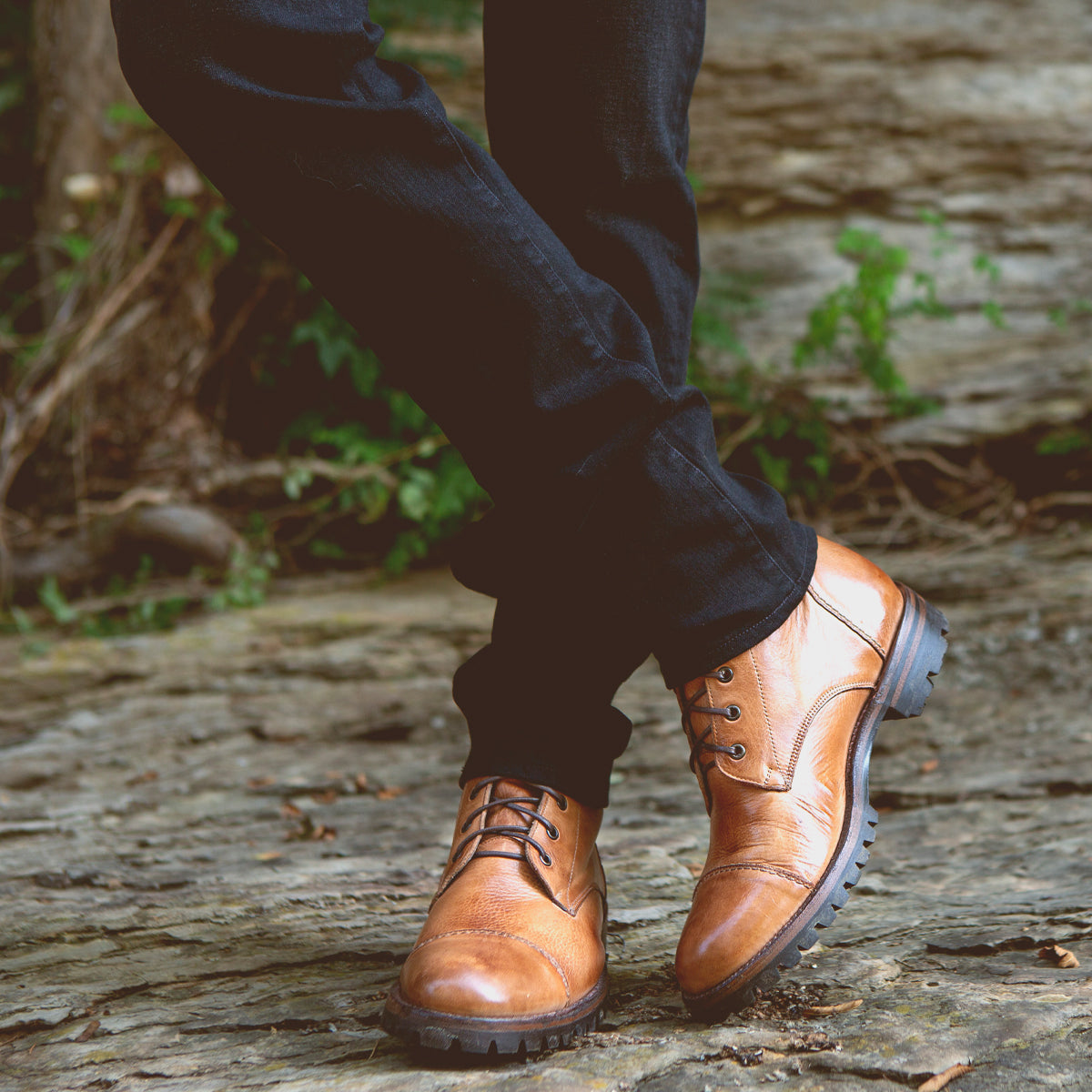 A person wearing Bed Stu Protege Trek two-tone leather boots walking on a cobblestone path.