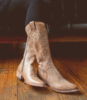 A Bed Stu Queen wearing a pair of tall tan boots adorned with fleur-de-lis designs.