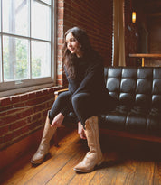 A woman sitting on a couch wearing Bed Stu tall cowboy boots named Queen.