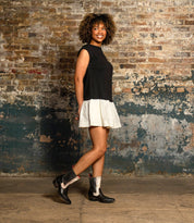 A woman stands sideways against a brick wall, smiling at the camera and showcasing her modern style in the Bed Stu "Raise" boots—sleek Western-inspired footwear in black and white.