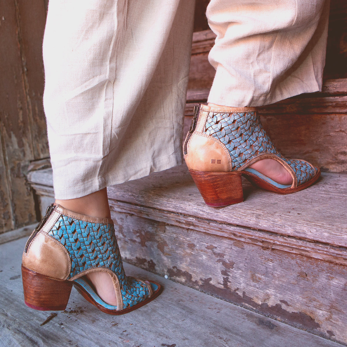 A person wearing stylish blue patterned handmade peep-toe ankle boots on a weathered wooden step.
