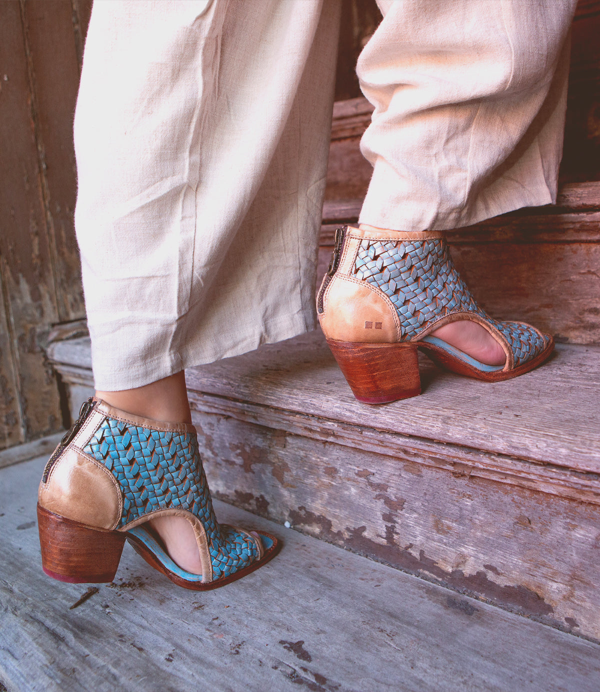 A person wearing stylish blue patterned handmade peep-toe ankle boots on a weathered wooden step.