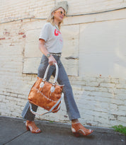 Woman walking by a wall carrying a large bag and wearing sunglasses, patterned pants, and Bed Stu artisan-crafted peep-toe heels.