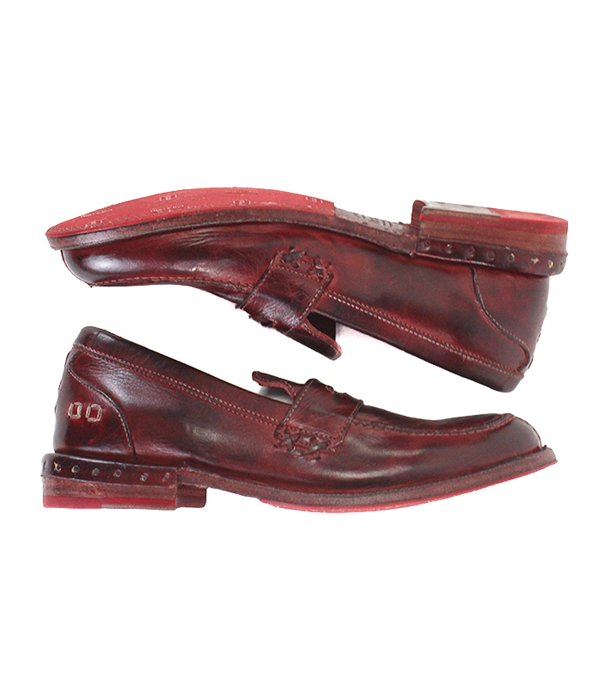 Two brown leather Reina loafers by Bed|Stü, crafted in a classic penny loafer style with red soles, are stacked sole-to-sole to showcase their visible stitching and Goodyear welted construction, as well as metal stud details on the heels.
