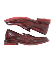 Two brown leather Reina loafers by Bed|Stü, crafted in a classic penny loafer style with red soles, are stacked sole-to-sole to showcase their visible stitching and Goodyear welted construction, as well as metal stud details on the heels.