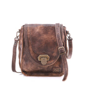 The Bed Stu Rhyme is a compact brown leather crossbody bag with a front flap, brass clasp, adjustable strap, and visible stitching—shown against a white background.
