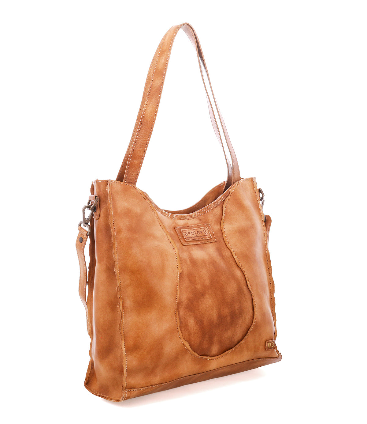 The Bed|Stü Ridgefield is a tan full-grain leather shoulder bag with a curved front pocket, dual handles, and subtle stitching, featuring an organized interior—photographed against a white background.