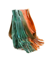 The Bed Stu Rimes tote, handcrafted in green and brown leather with long fringe details and a spacious interior, stands upright against a white background.